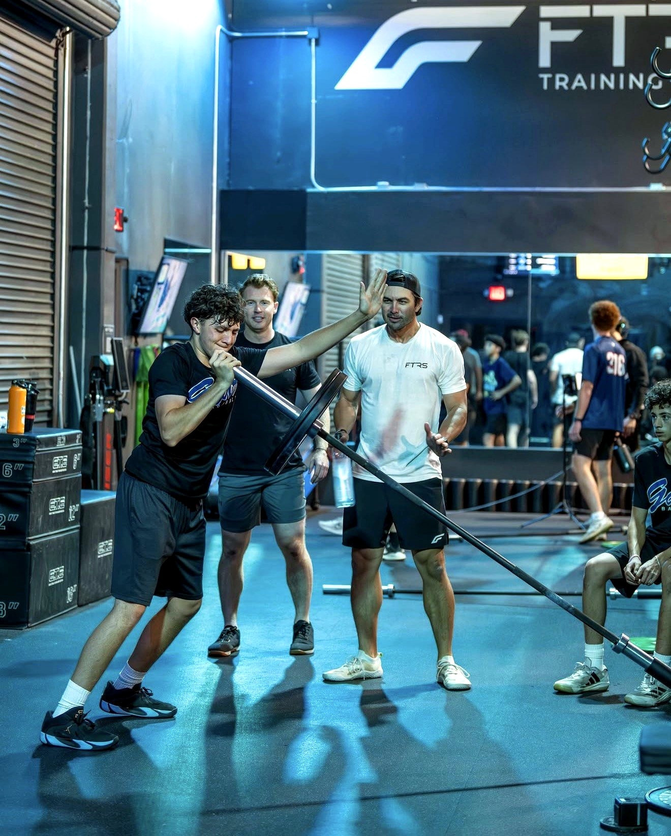 Coaches guide a young athlete through a barbell lift on the training floor at Futures Training Center.