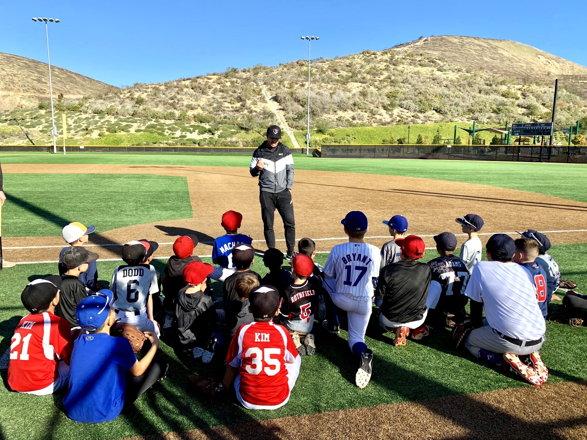 Chase d'Arnaud addresses a group of young players seated on a ballpark field.
