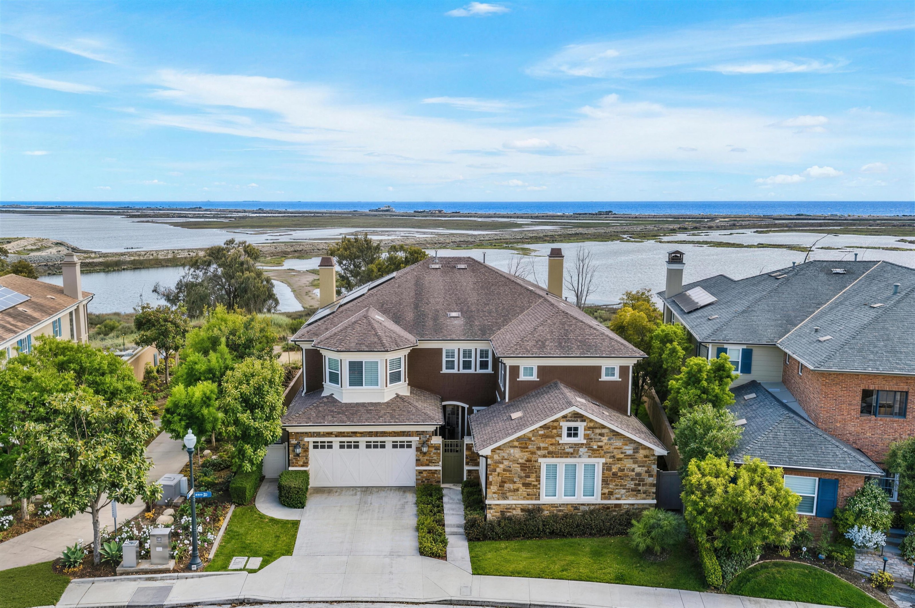 Aerial view of a two-story coastal residence with stone and brown siding beside a coastal marsh on Oceanridge Dr, Huntington Beach.